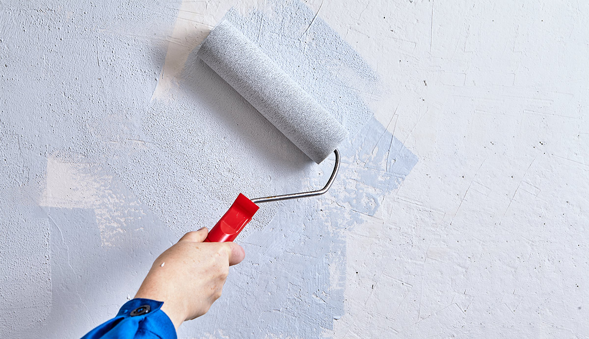 Home painter is painting walls with paint roller and paints during renovation